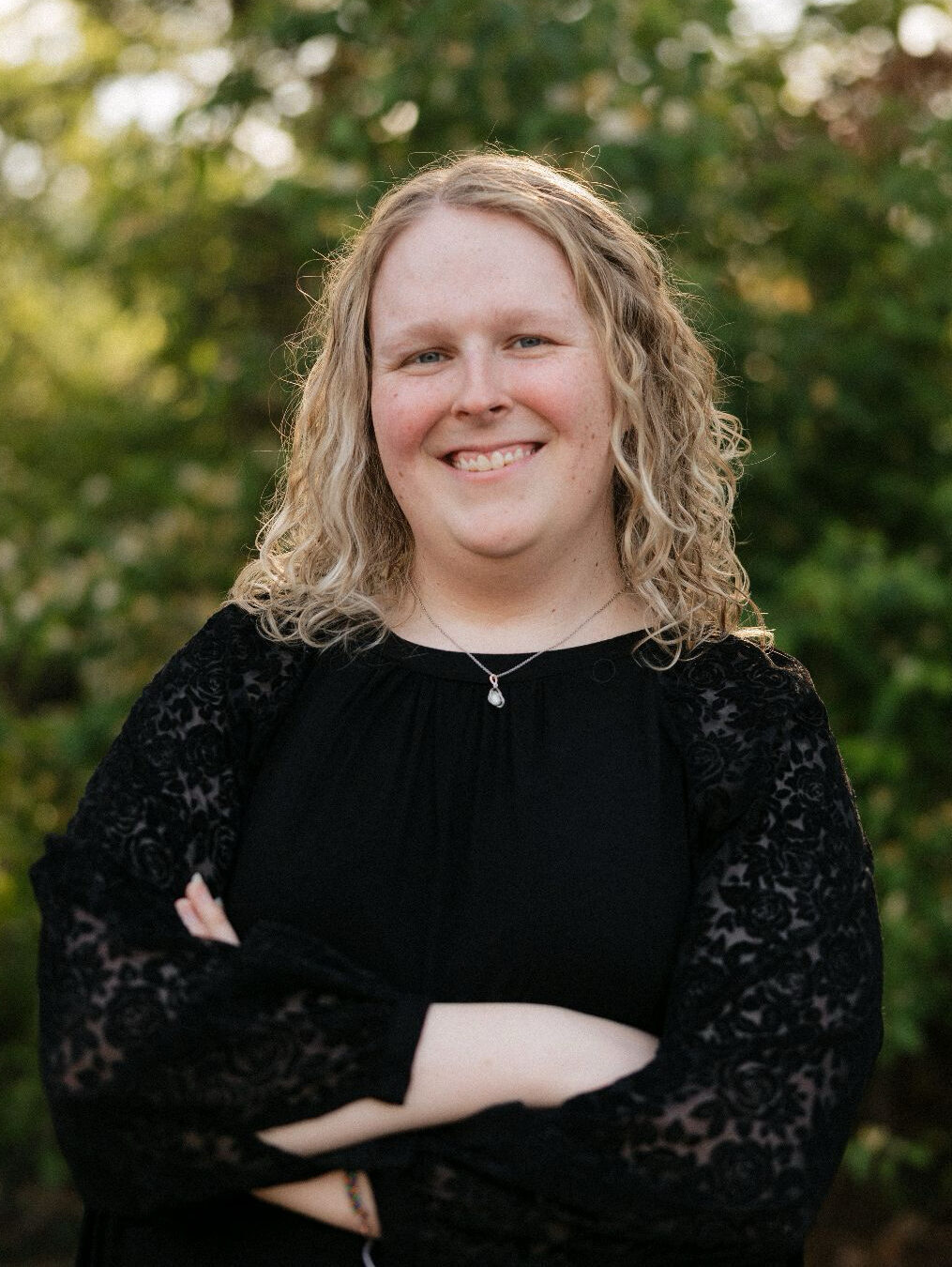 abbi-goins-ms-cmhc-therapist-nashville-tn Abbi Goins, MS-CMHC, therapist in Nashville, Tennessee, smiling outdoors with arms crossed in front of a green, natural background.