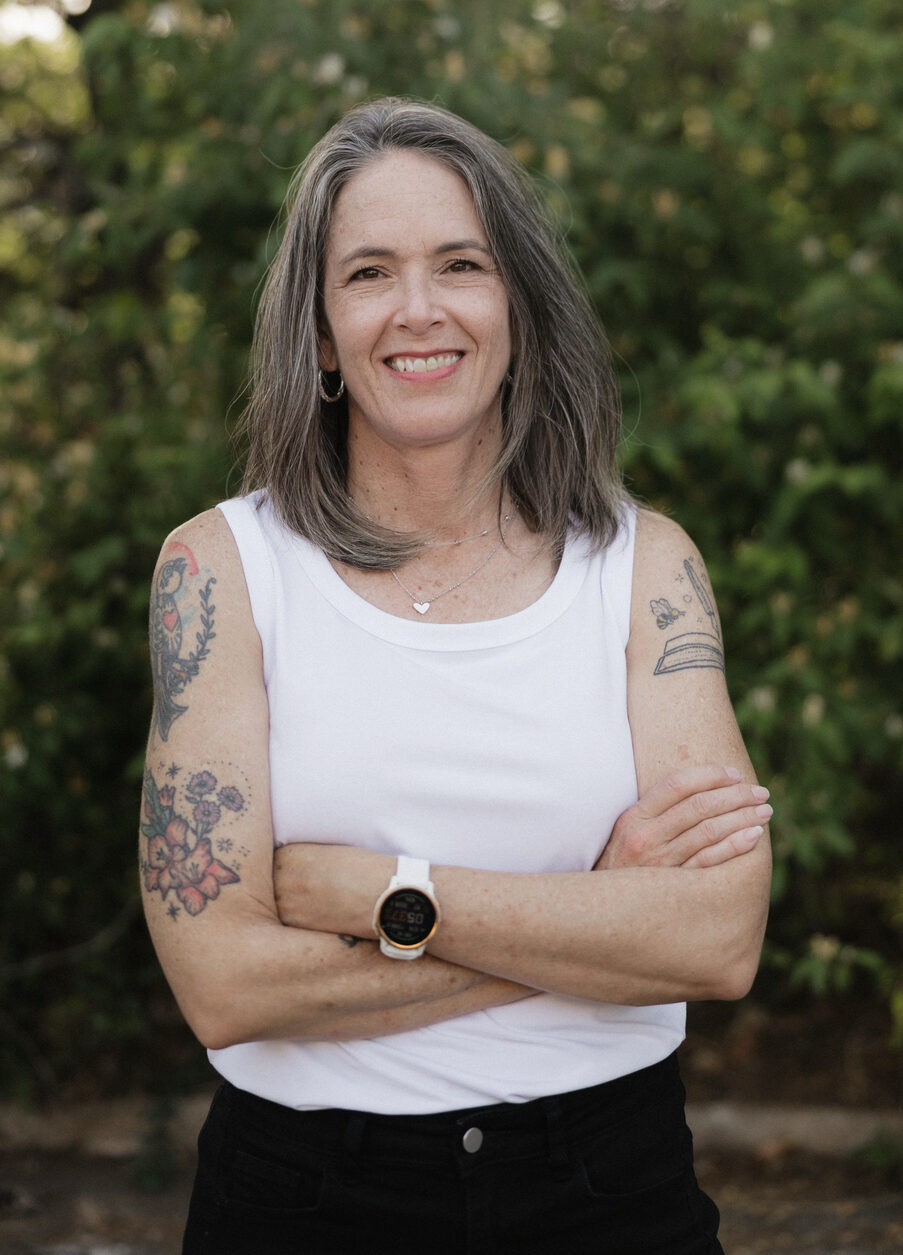 shelby-logsdon-lmft-therapist-nashville-tn Shelby Logsdon, LMFT, therapist in Nashville, Tennessee, standing outdoors with arms crossed and a green natural background.
