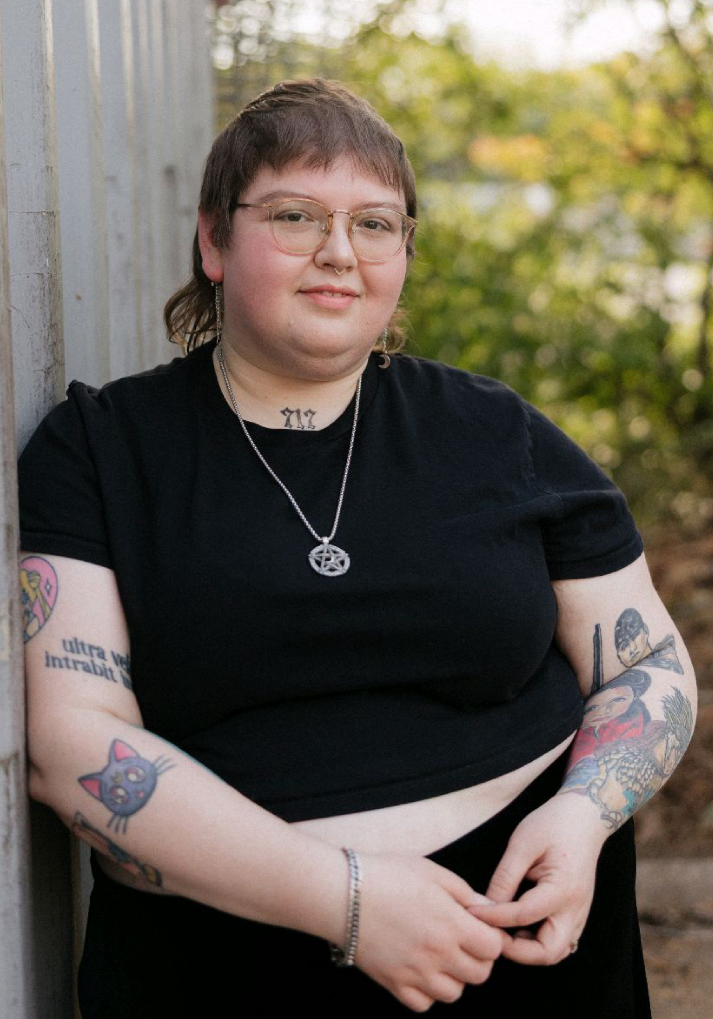 lydia-henderson-ma-atr-p-nashville-therapist Lydia Henderson, MA, ATR-P, art therapist in Nashville, Tennessee, standing outdoors beside a light-colored wall with greenery in the background.