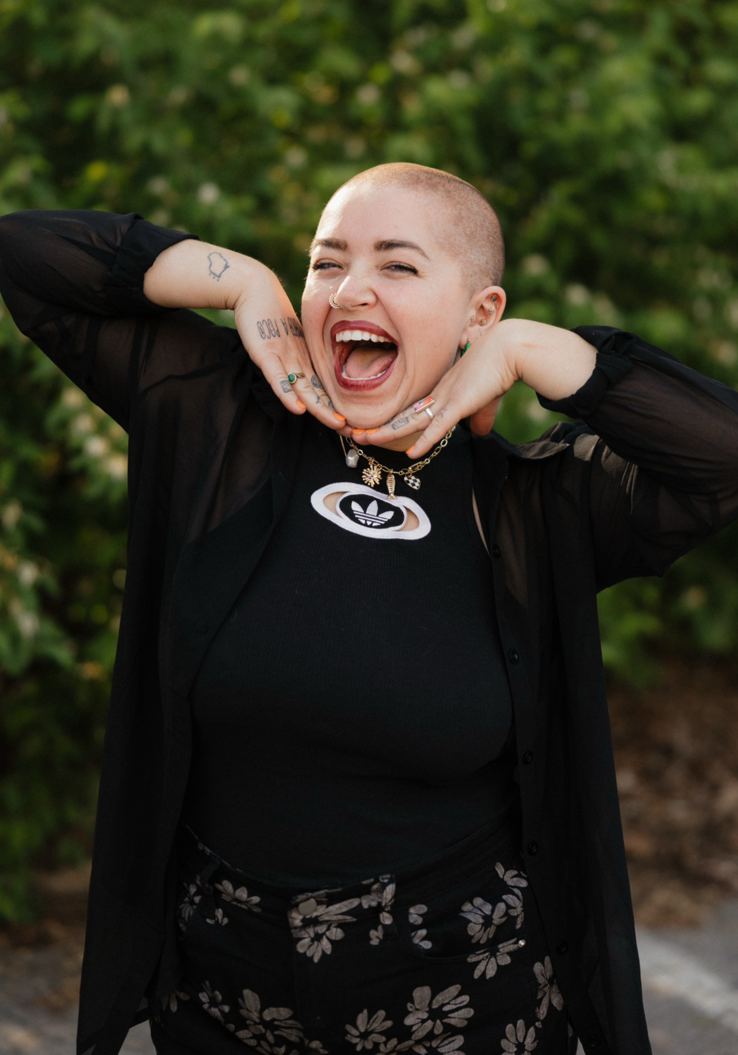 payton-lindner-mmft-nashville-therapist Payton Lindner, MMFT, therapist in Nashville, Tennessee, smiling outdoors with hands under their chin and greenery in the background.