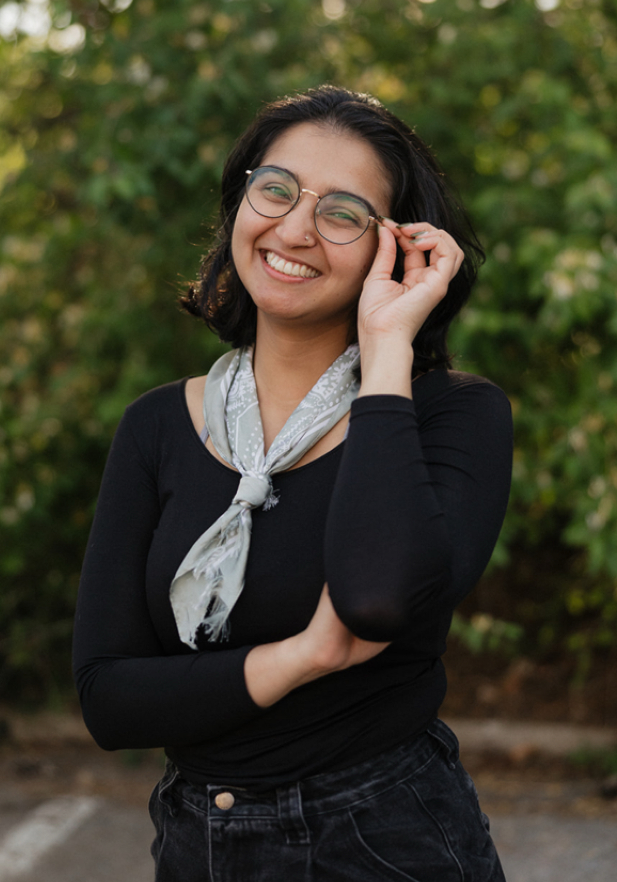 summer-sandhu-amft-nashville-therapist Summer Sandhu, therapist intern in Nashville, Tennessee, smiling outdoors and wearing glasses, with greenery in the background.